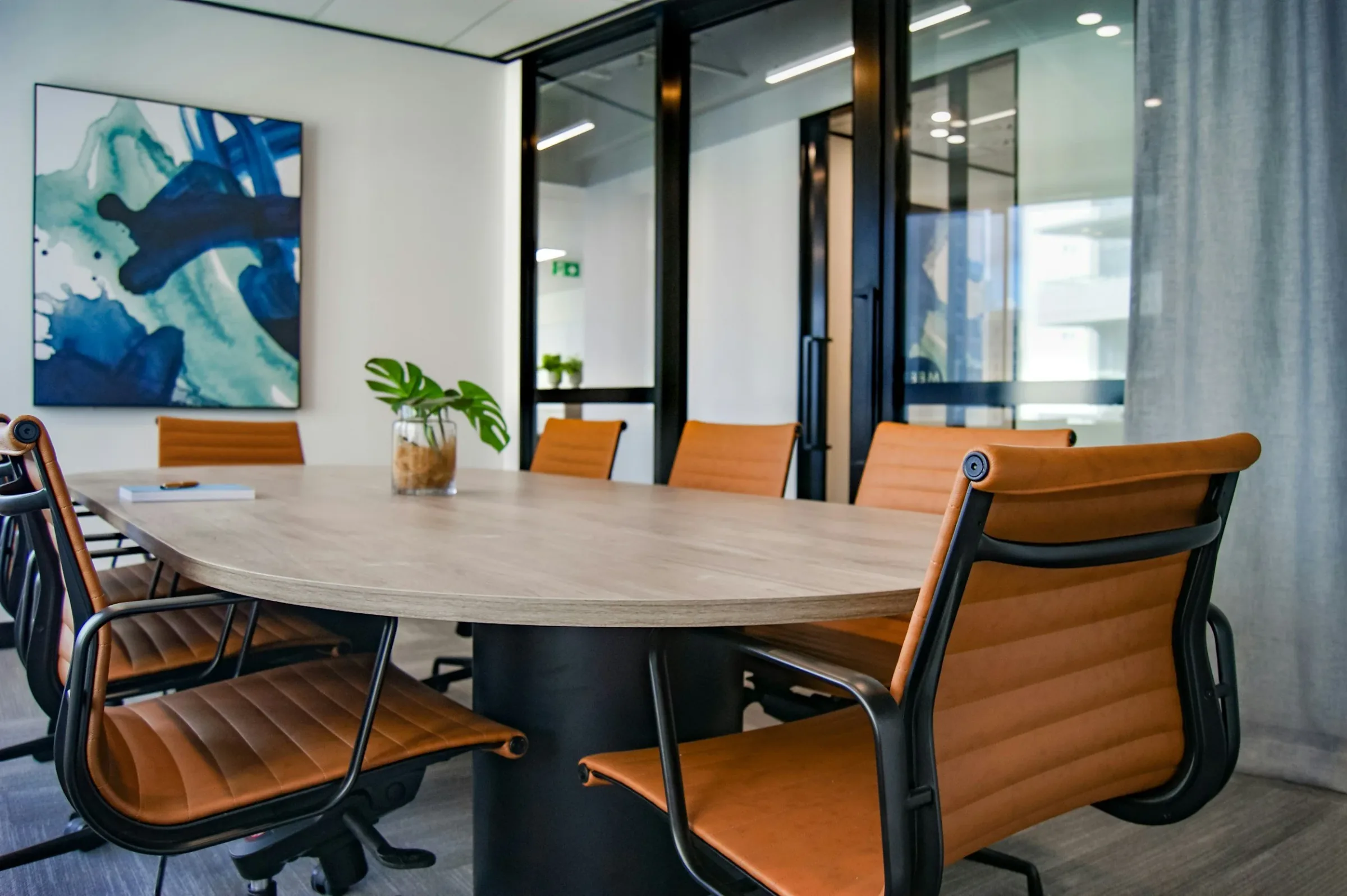 Modern conference room with oval table, orange leather chairs, and blue abstract artwork.
