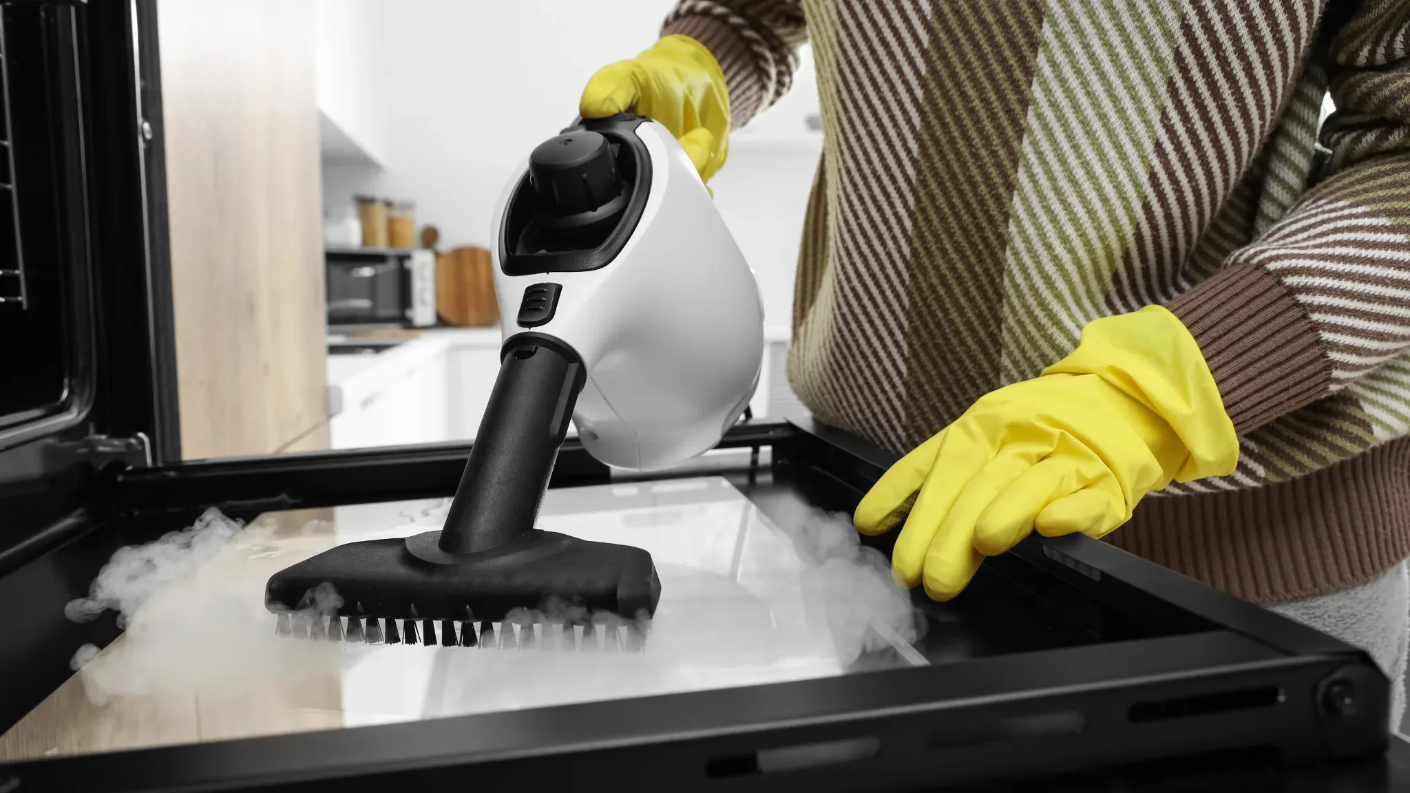 Professional house cleaner in yellow gloves using a steam cleaning machine with brush attachment on a kitchen stovetop, demon