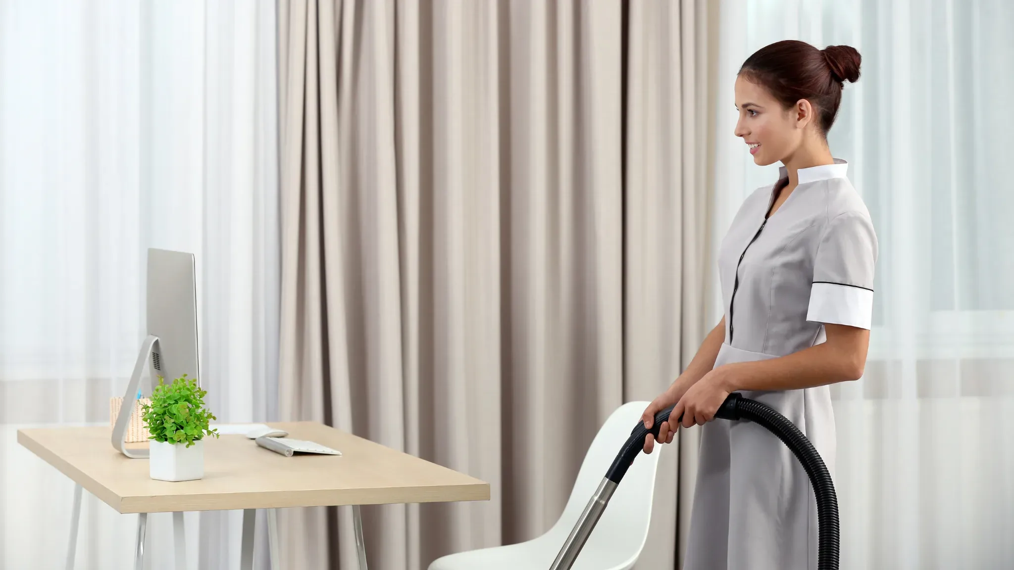 Professional house cleaning service worker using a vacuum cleaner in a modern home office space with neutral décor and natura