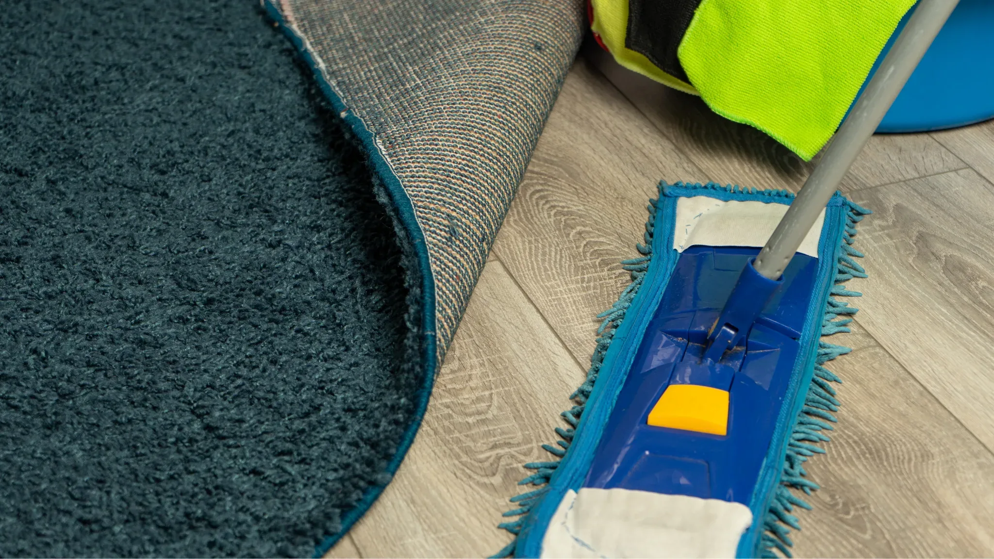 Professional mop cleaning hardwood floor next to teal carpet with cleaning supplies nearby